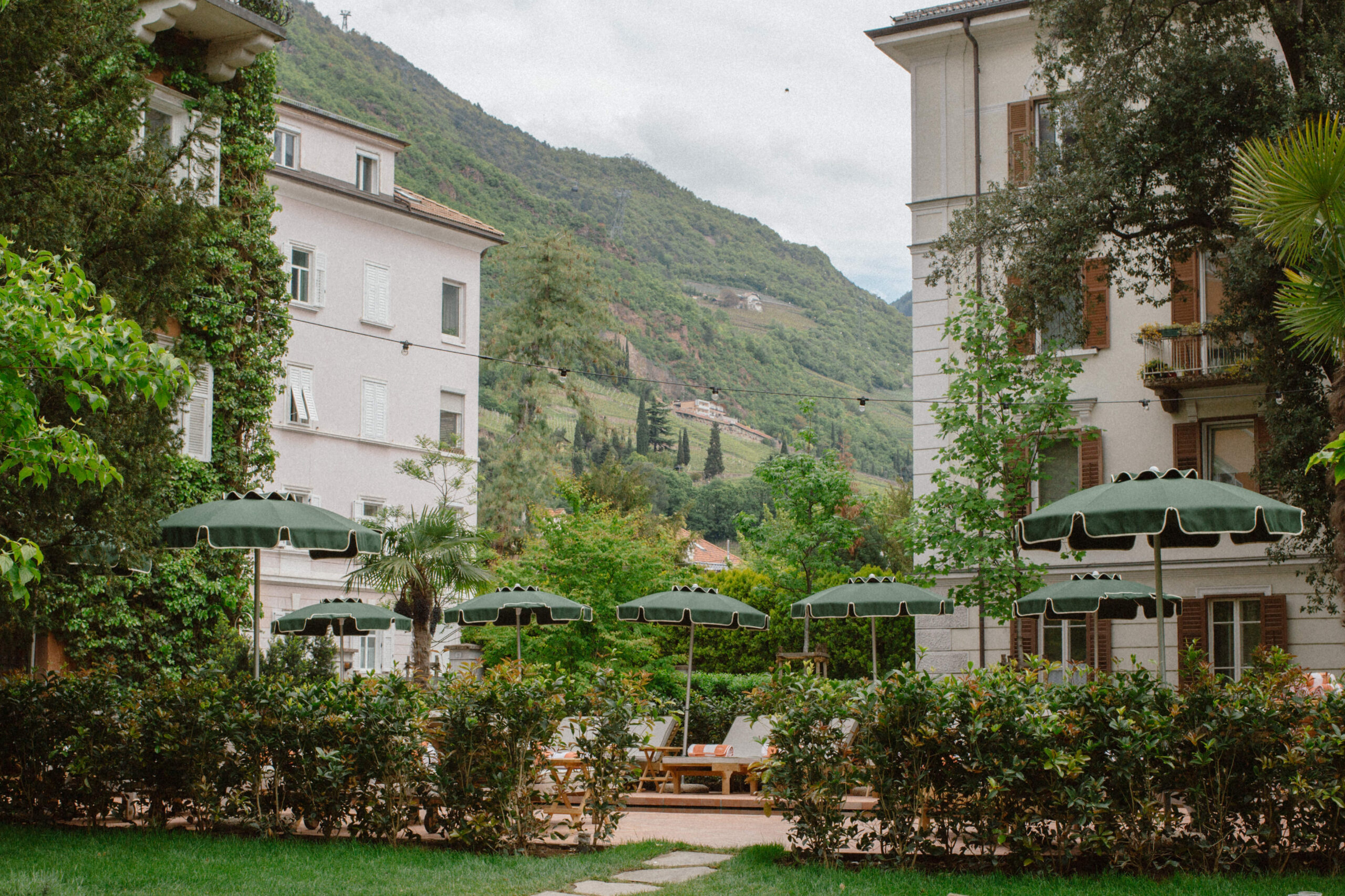 a view of a garden surrounded by mountains with green umbrellas in the foreground