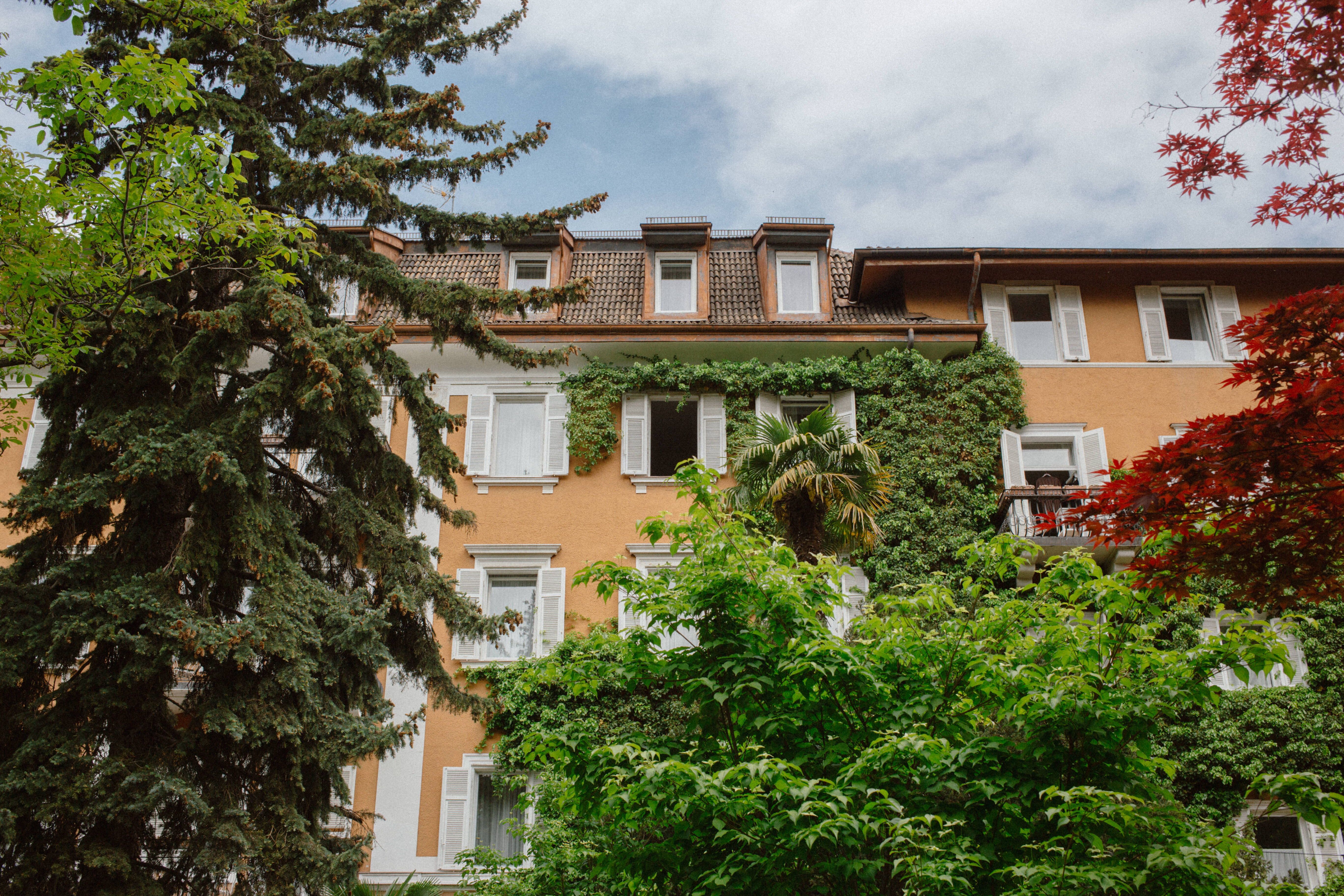 peach colored hotel with white window shutters and balconies in bolzano surrounded by trees