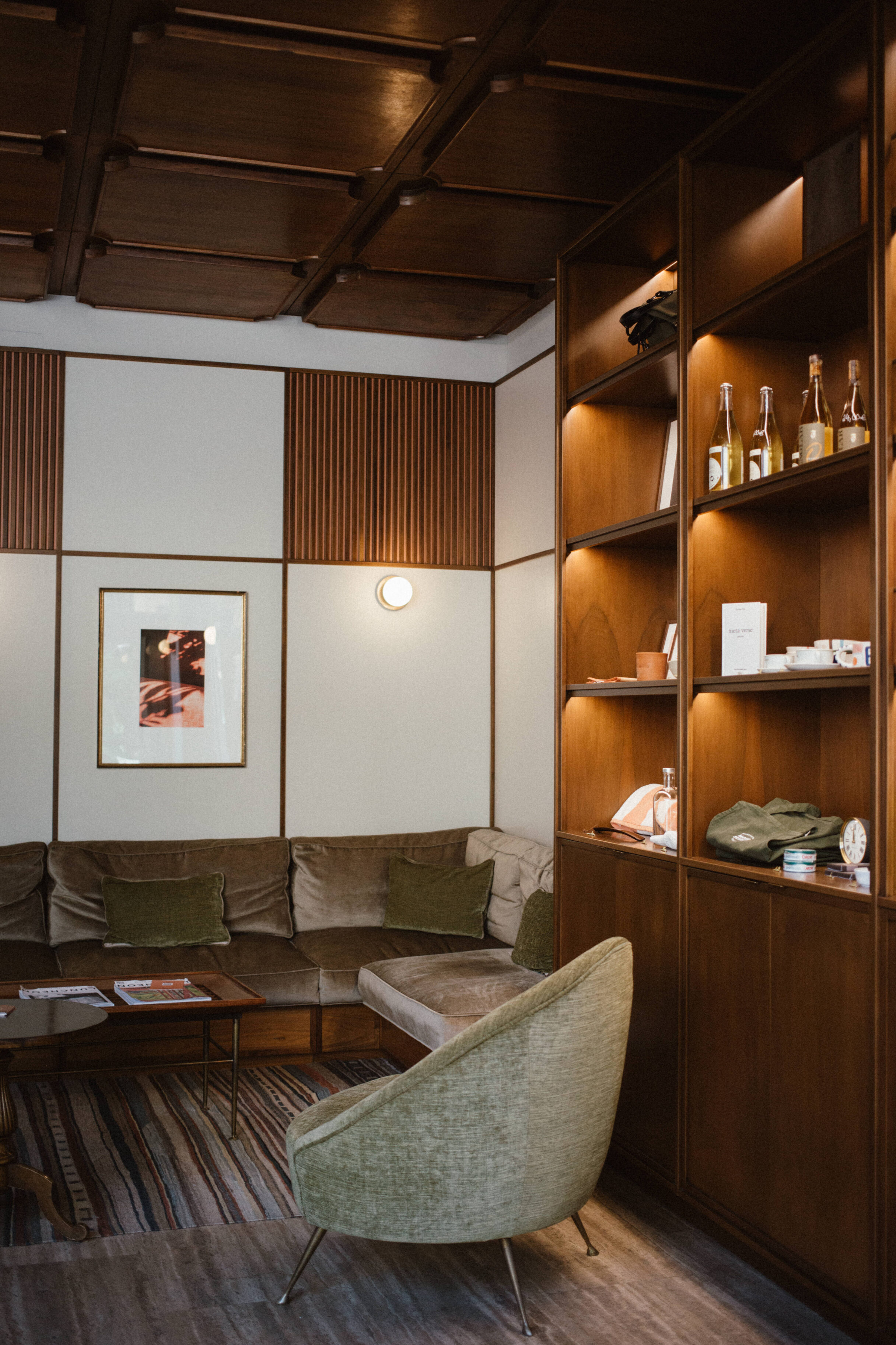 mid century modern hotel lobby with suede velvet brown and green couch details and shelf of goods like tote bags, towels, wine, and home decor items