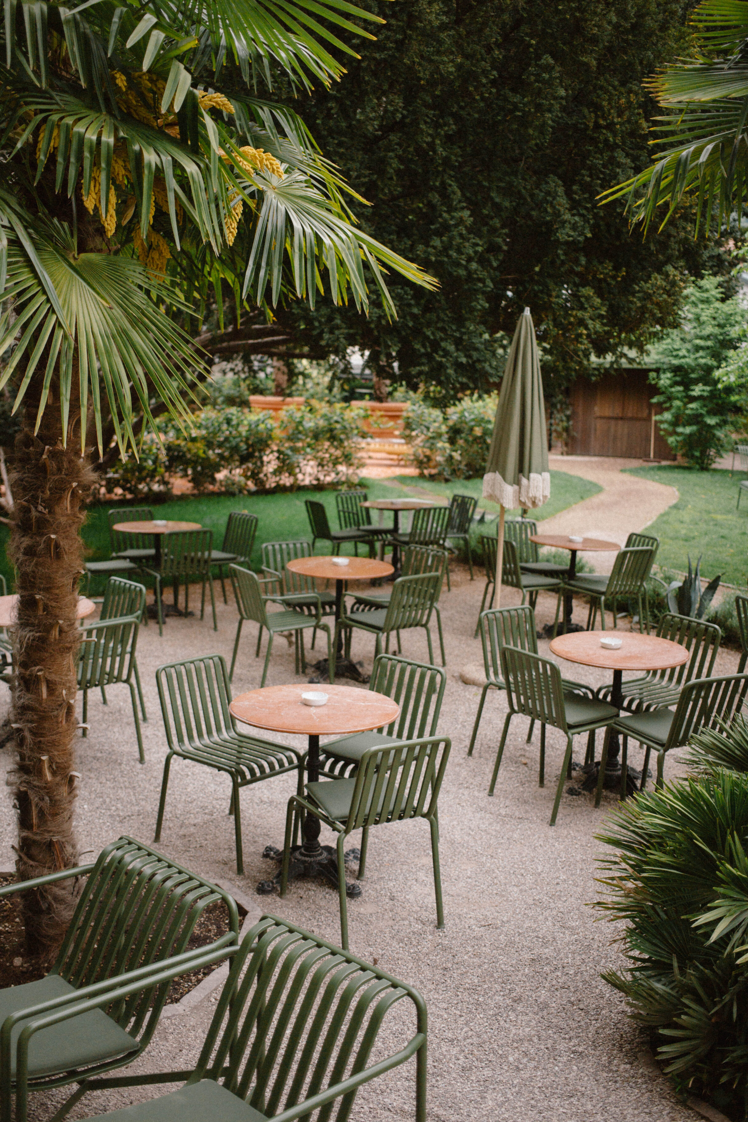 green metal chairs with pink marble cafe tables and white ashtrays in the middle of a lush park in bolzano, italy