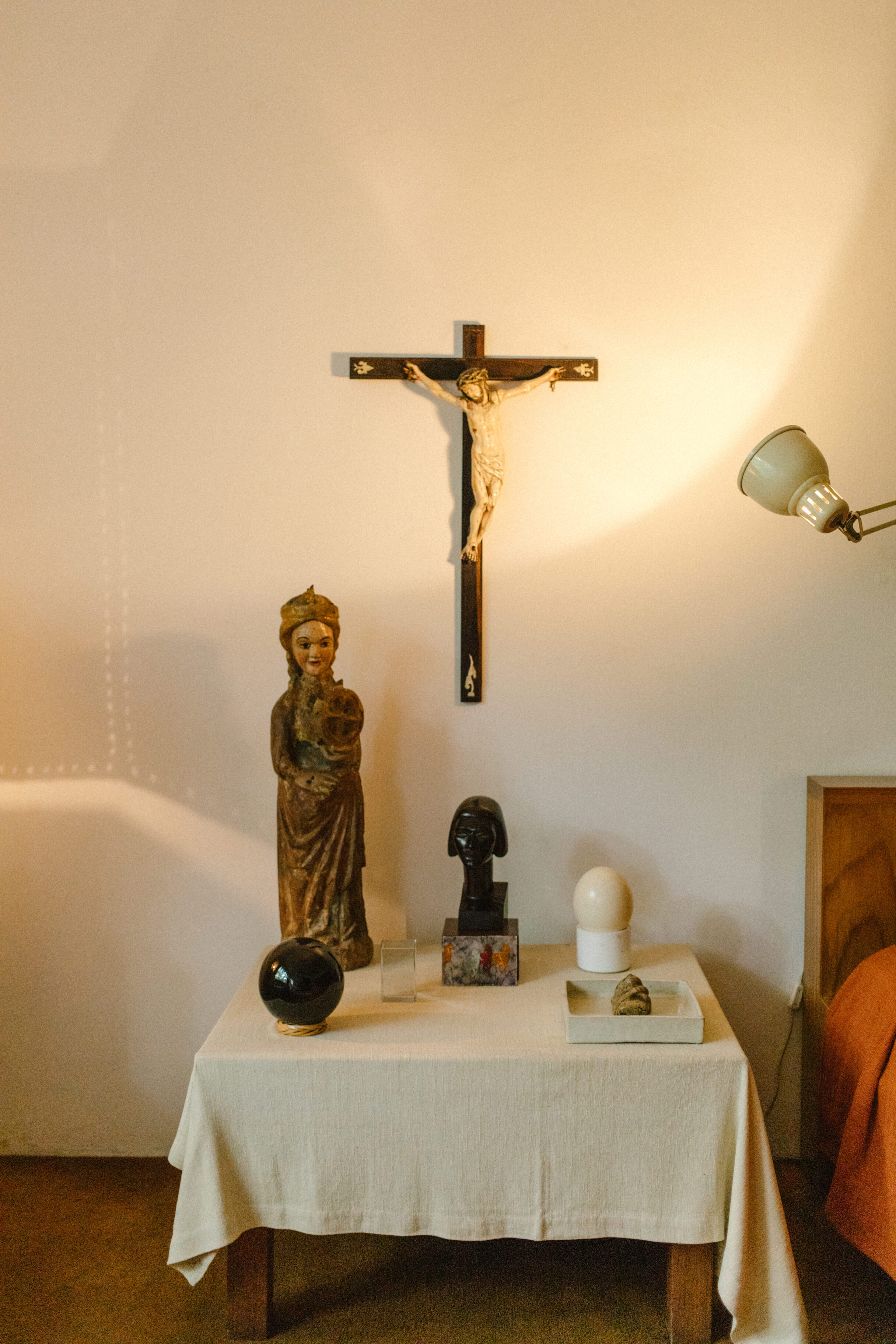 warm colored lamp pointed at a cross crucifix above a small table with tablecloth adorned with sculptures and other religious artifacts